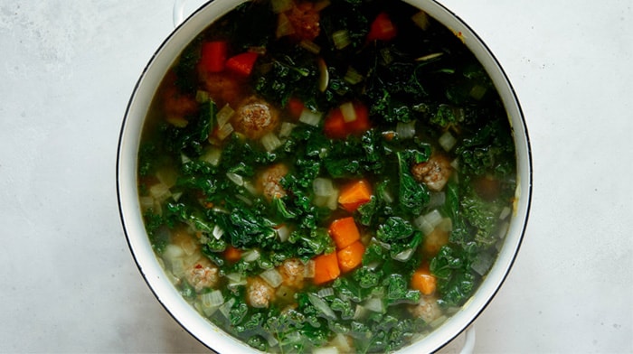 Tortellini soup in a stock pot on a kitchen counter.