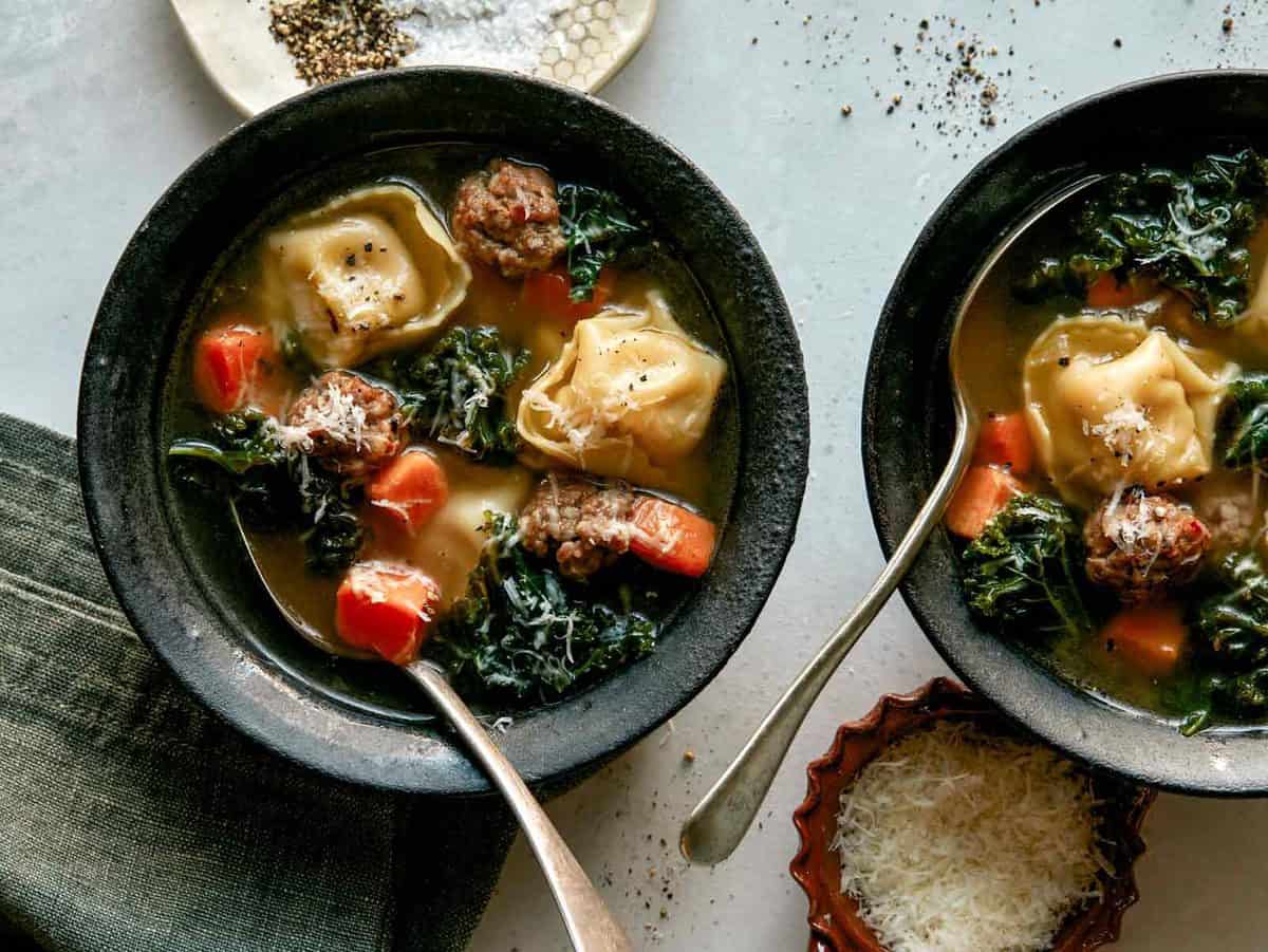 Tortellini soup in two bowls with spoons in them and a napkin nearby.