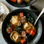 Tortellini soup in two bowls with spoons in them and a napkin nearby.