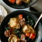 Tortellini soup in two bowls with spoons in them and a napkin nearby.