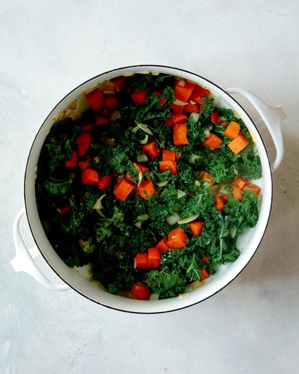 Kale, sweet potatoes, and onions in a stock pot cooking to make tortellini soup.