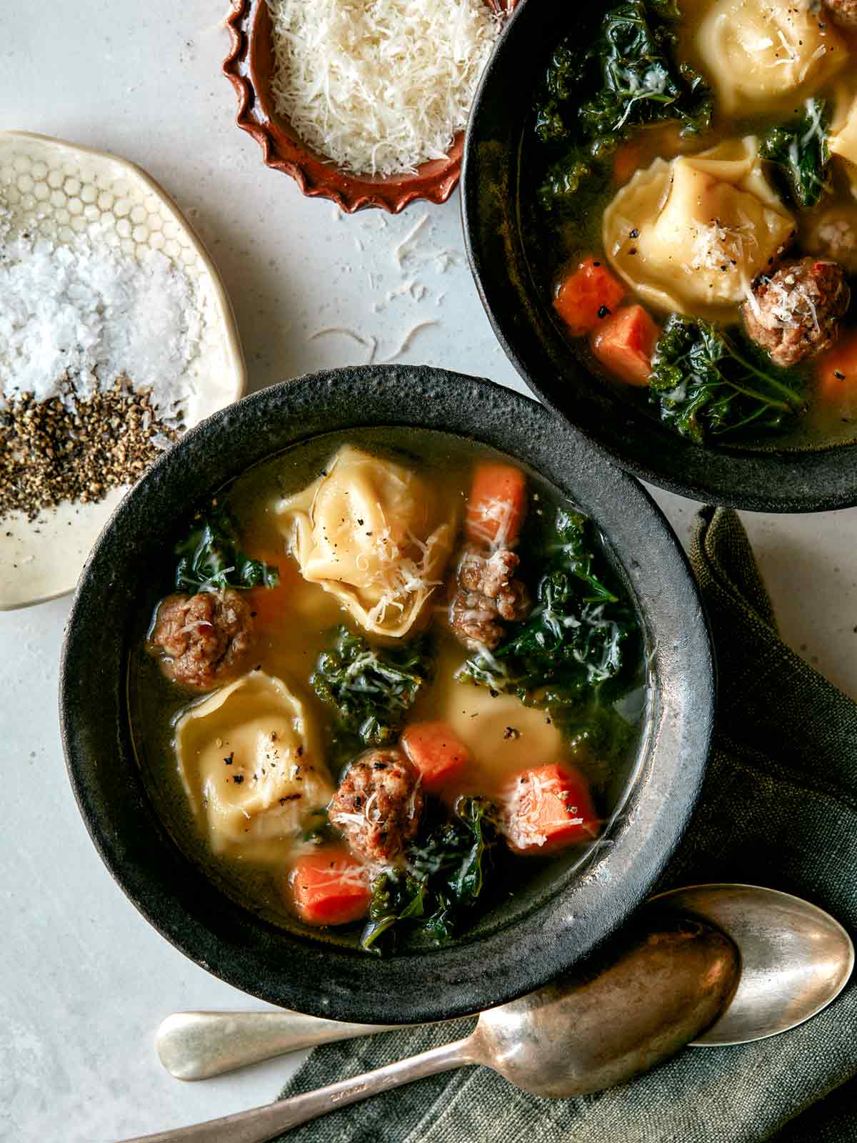 Tortellini Soup recipe in two bowls with parmesan next to it. 