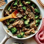 Beef and broccoli in a skillet with plates on the side.