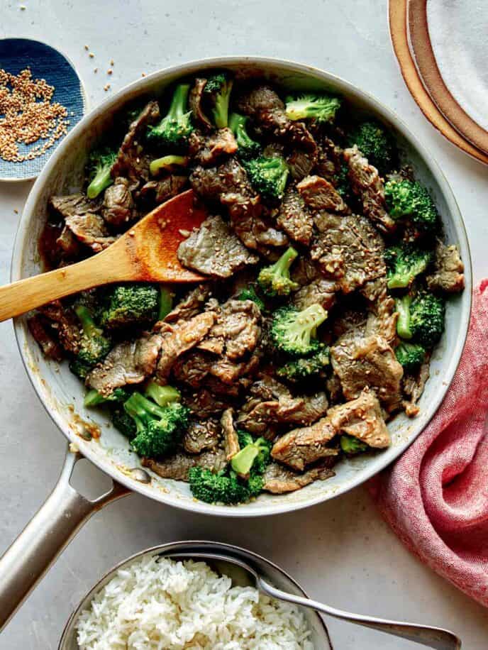 Beef and broccoli in a skillet with plates on the side.