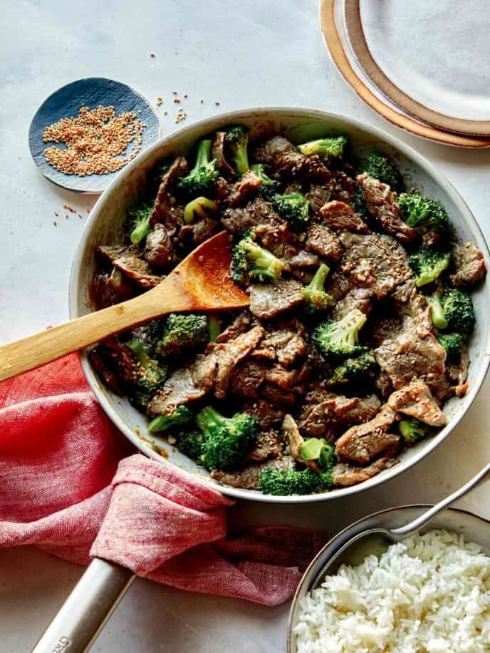 Beef and broccoli in a skillet with rice on the side. 
