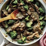 Beef and broccoli in a skillet with plates on the side.