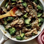 Beef and broccoli in a skillet with plates on the side.