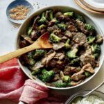 Beef and broccoli in a skillet with plates on the side.