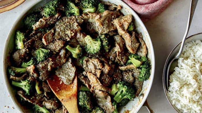 Beef and broccoli in a skillet with plates on the side.