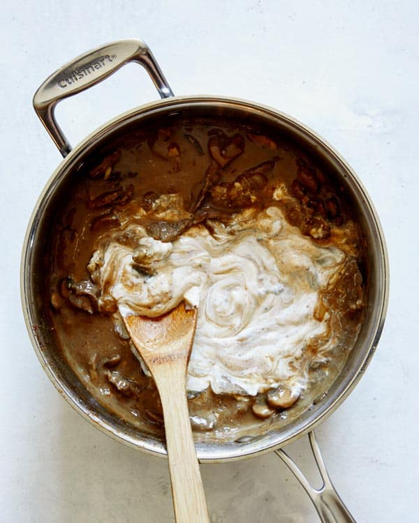 Sour cream being mixed into beef stroganoff mixture.