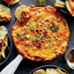 Buffalo chicken dip in a skillet with chips and veggies on the side.