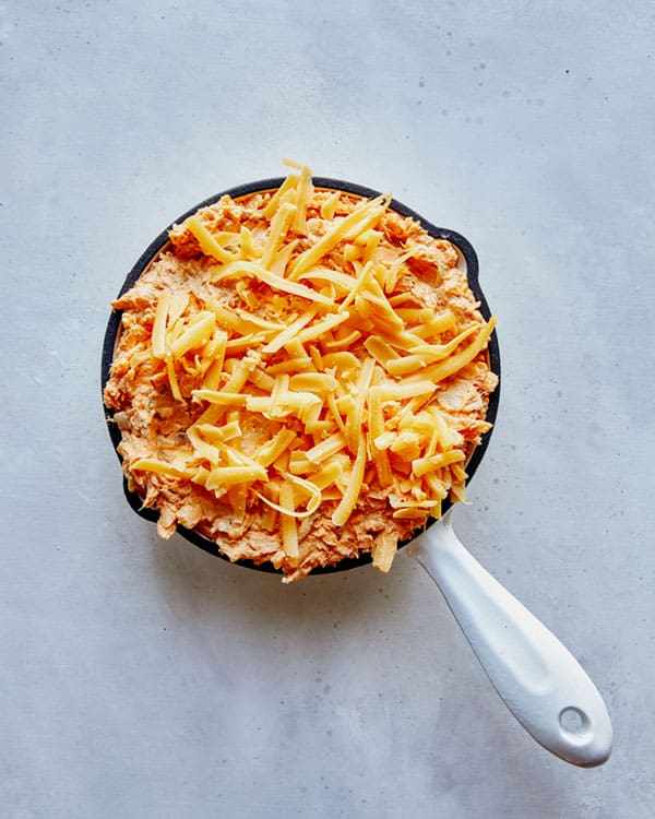 Cheese sprinkled on top of a skillet filled with buffalo dip.