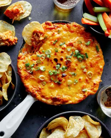 Buffalo chicken dip in a skillet with chips and veggies on the side.