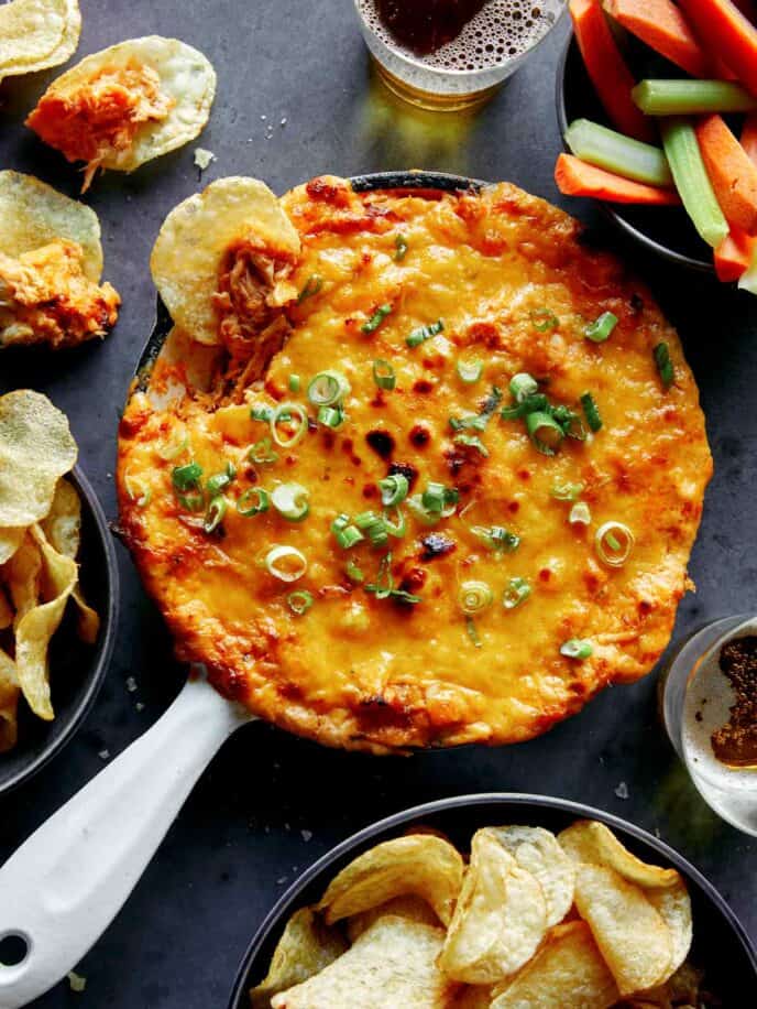 Buffalo chicken dip in a skillet with chips and veggies on the side.