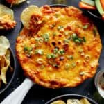 Buffalo chicken dip in a skillet with chips and veggies on the side.