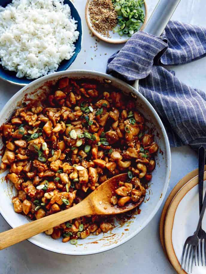 Cashew chicken recipe in a skillet with plates and forks on the side. 