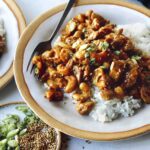 Cashew chicken with on two plates with forks and rice.