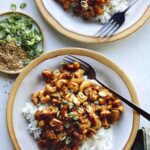 Cashew chicken with on two plates with forks and rice.