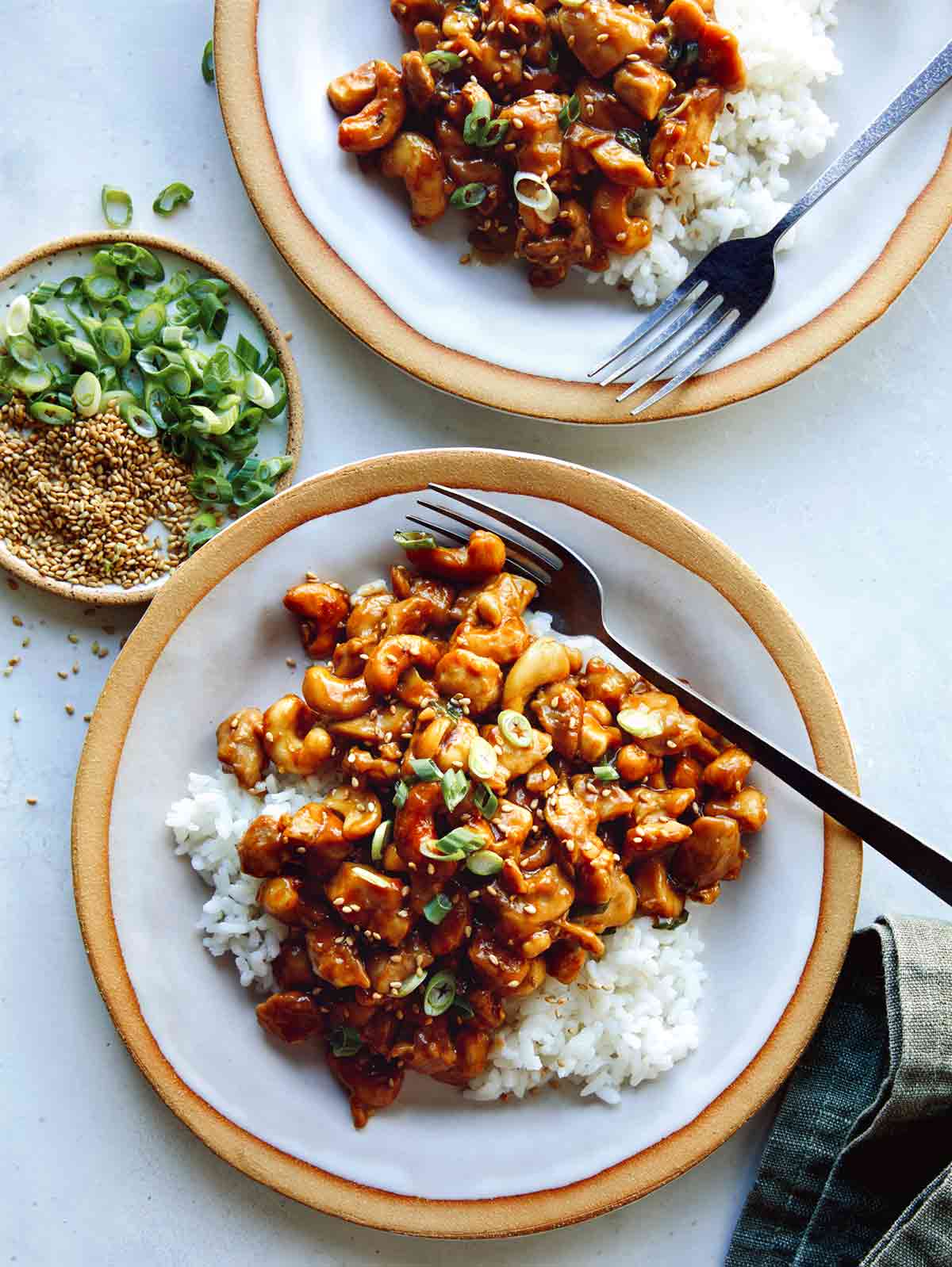 Cashew chicken with on two plates with forks and rice.