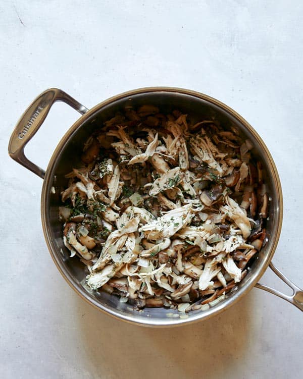 Chicken and mushrooms in a skillet with onions.