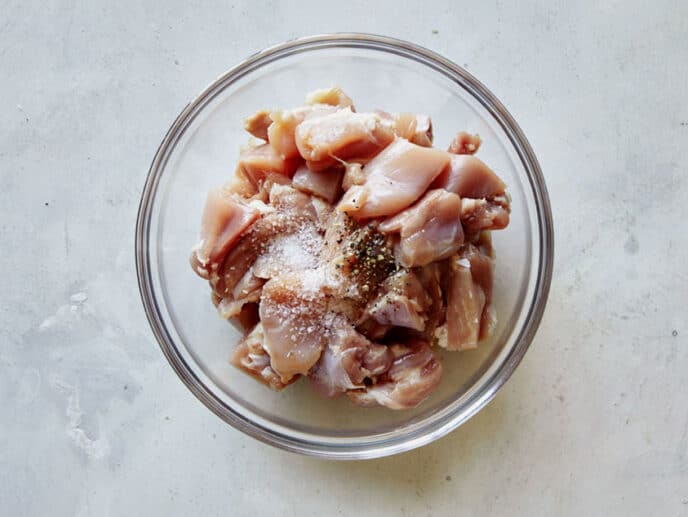 Chicken thighs in a bowl with salt and pepper on top.