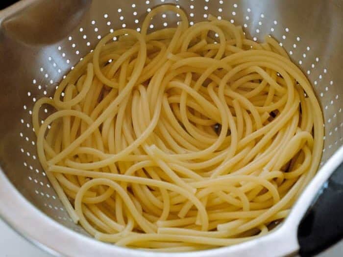 Cooked bucatini noodles in a strainer.