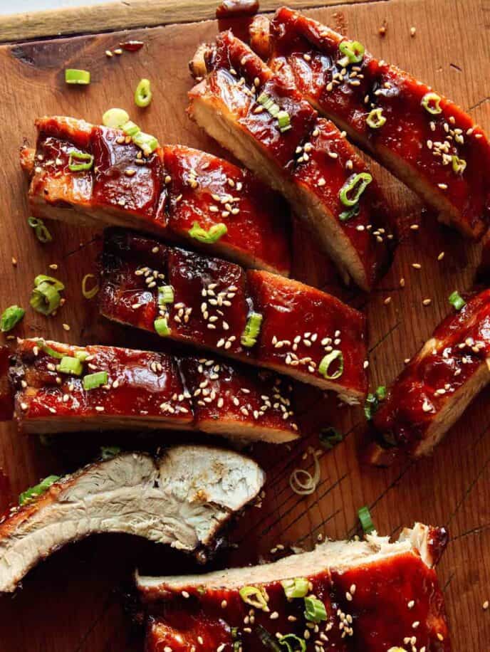 Oven baked sticky ribs with sesame seeds and green onions on a cutting board.