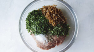 Ground lamb with seasoning in a glass bowl to mix together.
