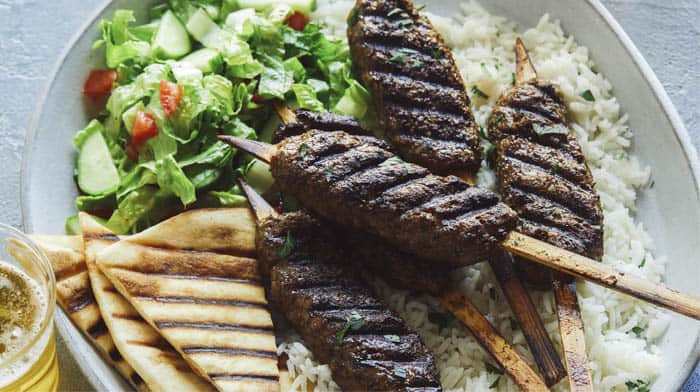 Lamb kofta skewers on a platter with pita and rice.