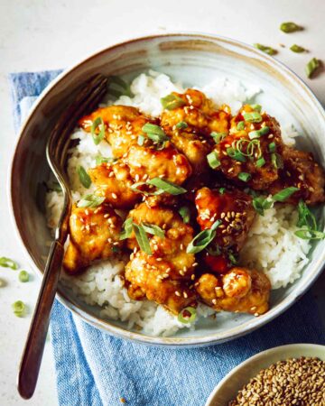 Bowl of sesame chicken on white rice with a fork.