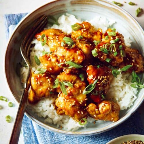 Bowl of sesame chicken on white rice with a fork.