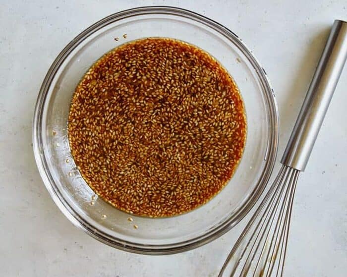 A bowl of sesame chicken sweet and sticky sauce in a mixing bowl with a whisk next to it.