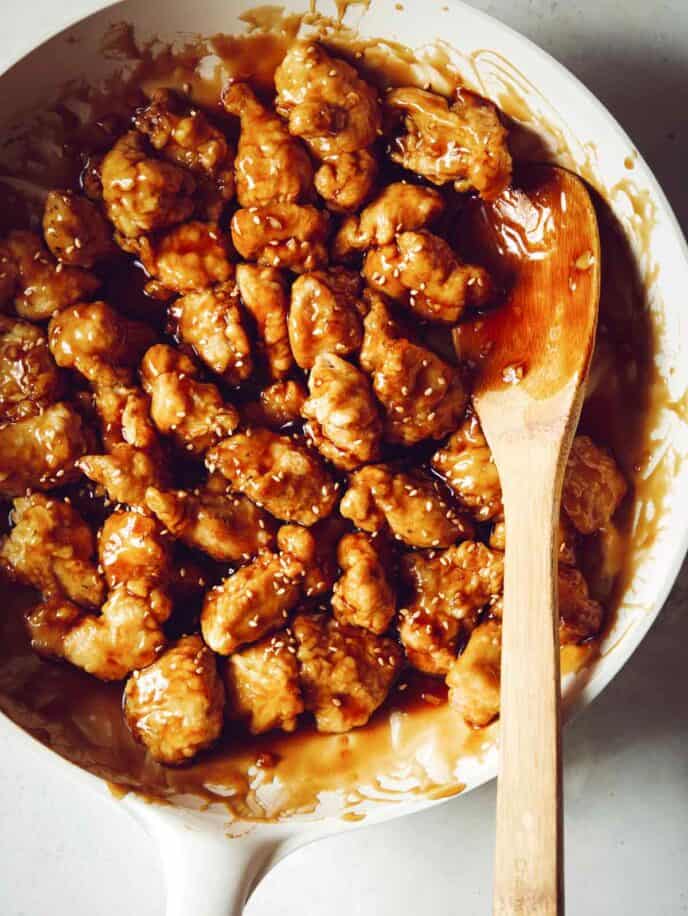 A skillet of sesame chicken tossed in a sauce. 