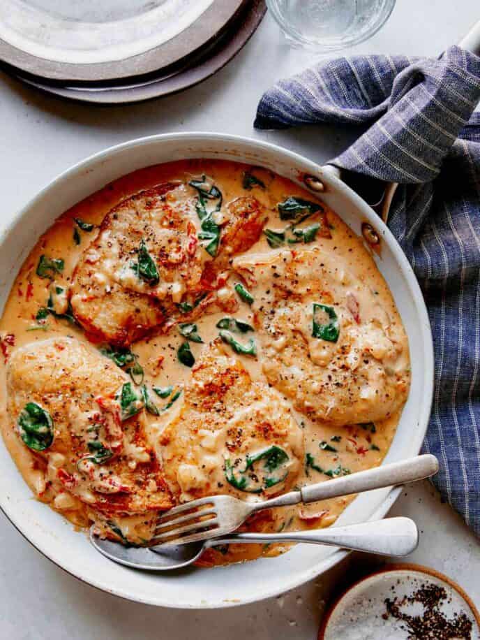 Tuscan chicken recipe in a skillet with plates on the side.
