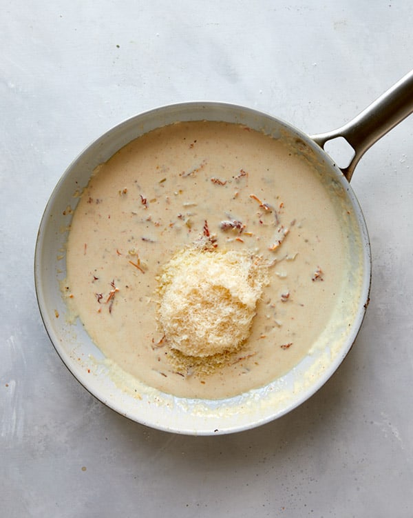 Adding parmesan to sauce in a skillet for tuscan chicken.