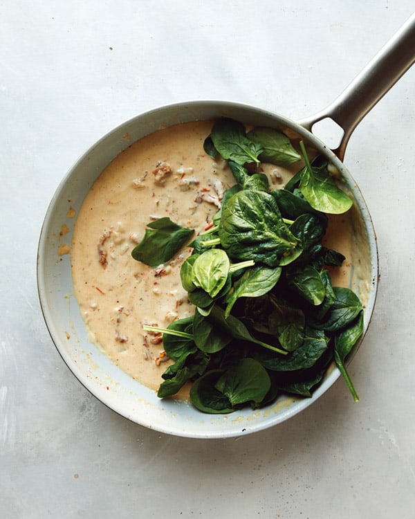 Adding spinach to tuscan chicken sauce in a skillet.