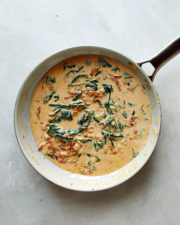 Cooking spinach into tuscan chicken sauce.