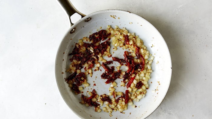 Onions and sun dried tomatoes cooking in a skillet to make Tuscan Chicken.
