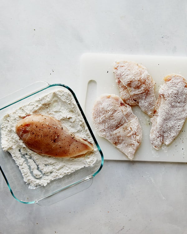 Chicken breasts being dredged in flour to make tuscan chicken.