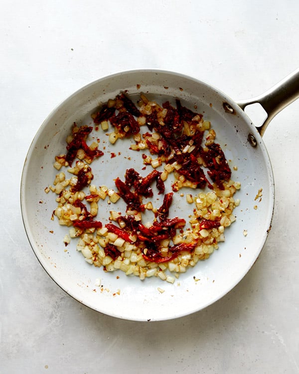Onions and sun dried tomatoes cooking in a skillet to make Tuscan Chicken.