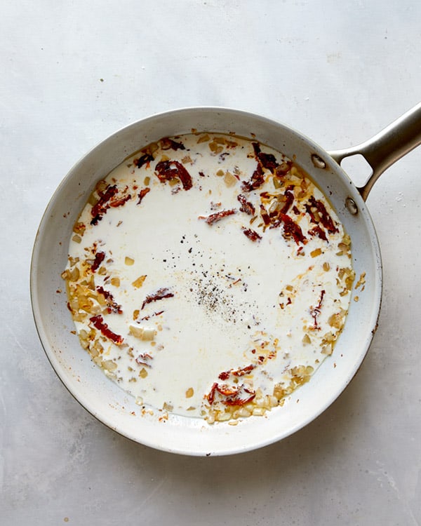 Cream with onions and sun dried tomatoes in a skillet to make Tuscan Chicken.