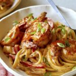Two bowls of cajun shrimp pasta with green onions on top.