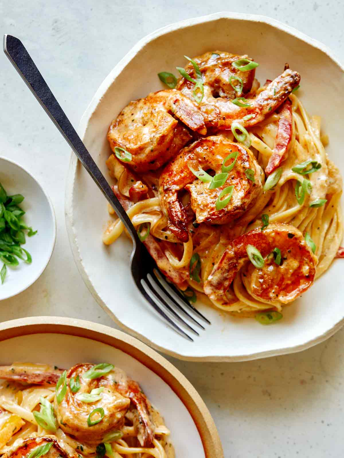 Cajun shrimp pasta in two bowls with green onions on the side. 