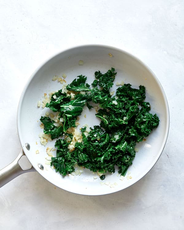 Kale with onions and garlic cooking in a skillet.