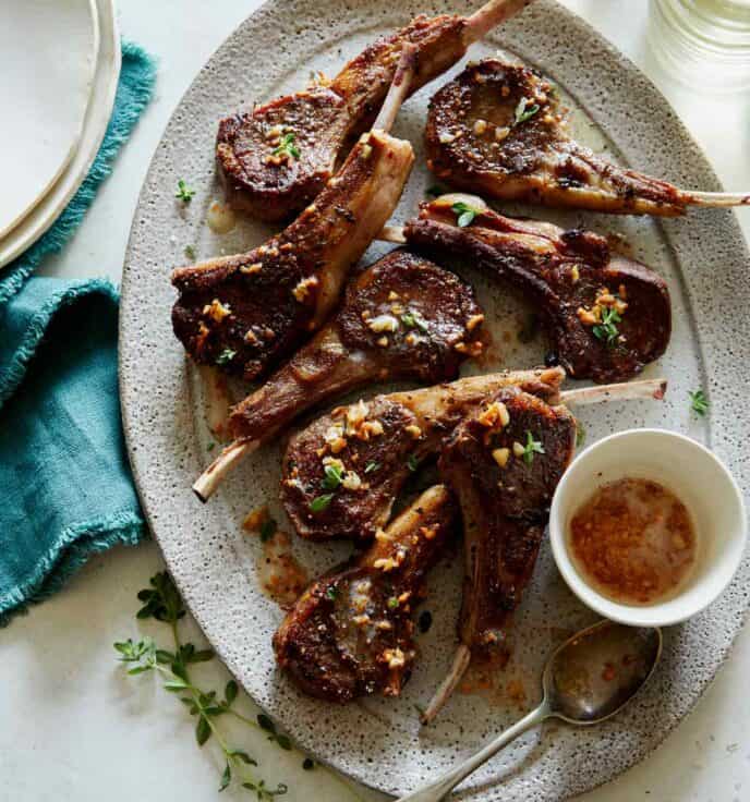 Garlic butter lamb chops recipe on a platter with plates next to it.