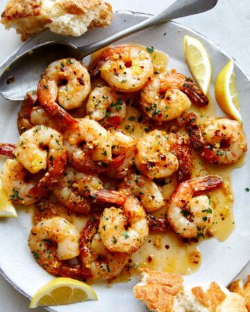 Shrimp scampi recipe on a plate with bread and lemon wedges.