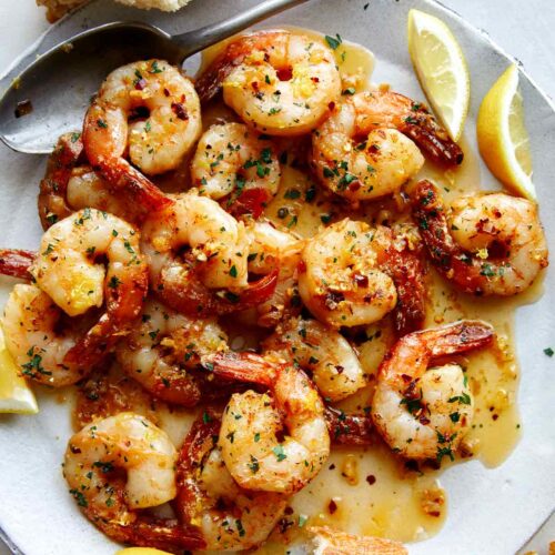 Shrimp scampi recipe on a plate with bread and lemon wedges.