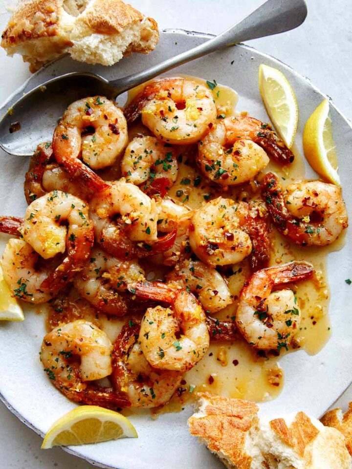 Shrimp scampi recipe on a plate with bread and lemon wedges.