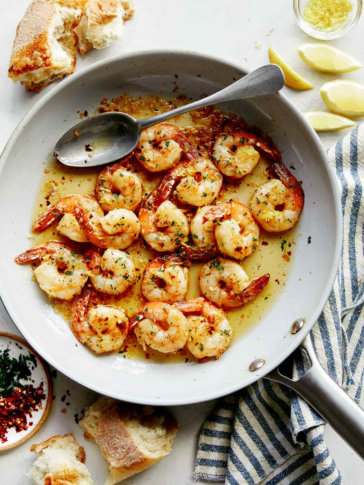 Shrimp scampi in a skillet with lemon wedges. 