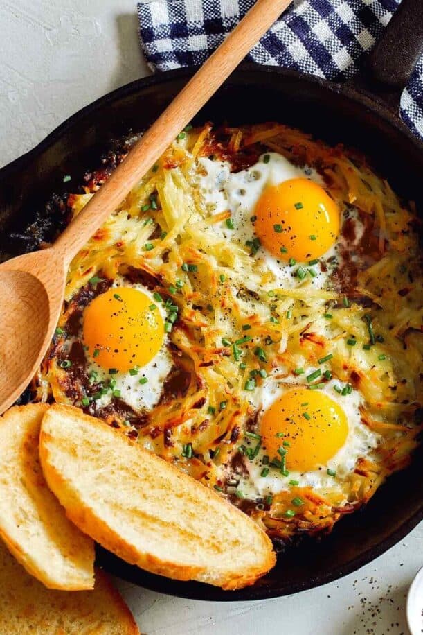 Simple cheesy skillet hash browns and eggs with bread and a wooden spoon.